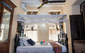 A bedroom with a canopy bed, a ceiling fan, and a window with bars.