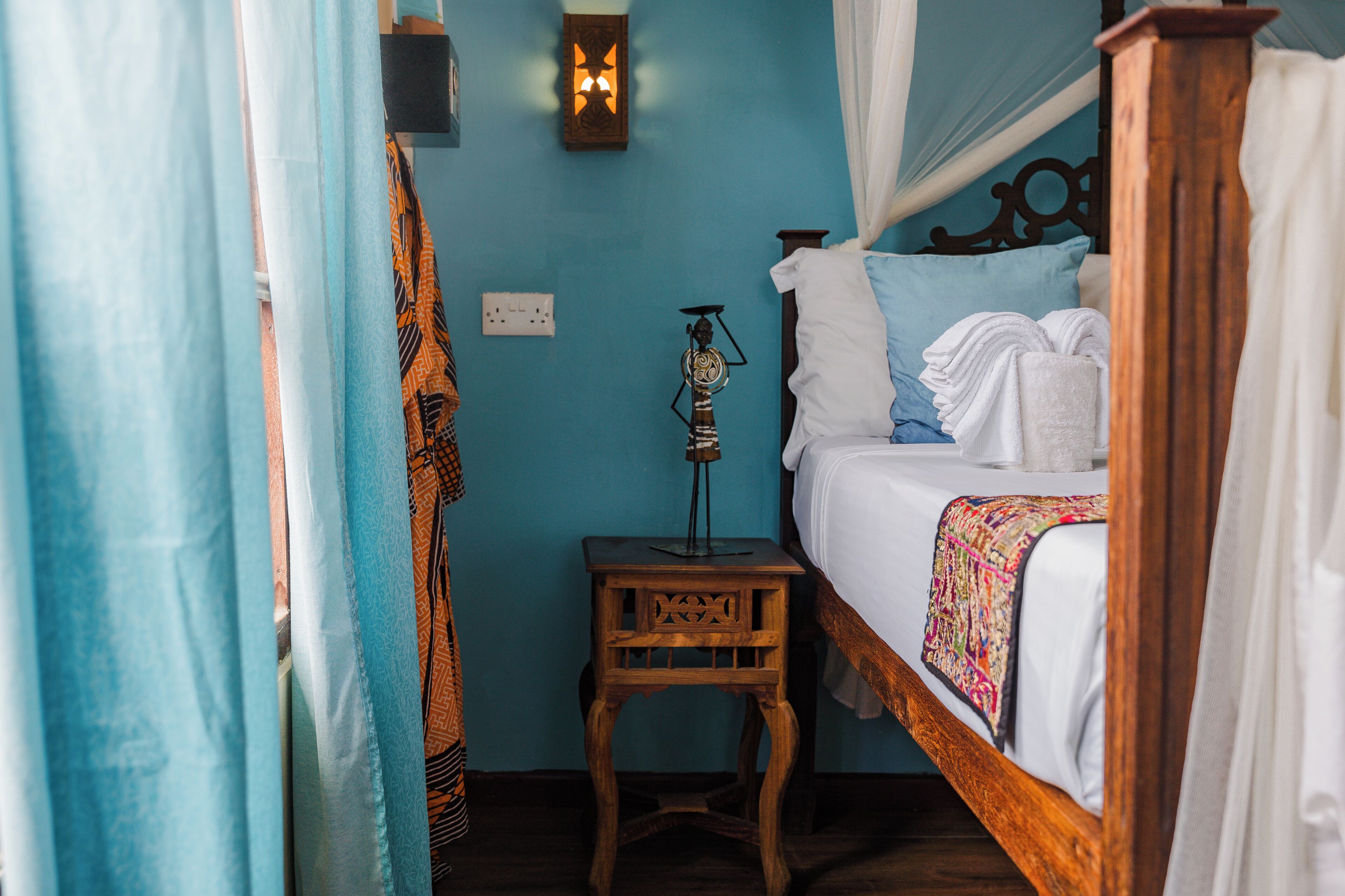 A bedroom with a wooden bed, a nightstand, a wall-mounted lamp, and a blue wall.