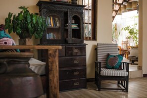 A room with a dark wooden cabinet with books, a potted plant, and a striped chair with a cushion.