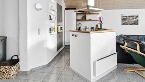 Eine kompakte Küche mit integriertem Kühlschrank, einer Holz Arbeitsplatte und einer Pendelleuchte.