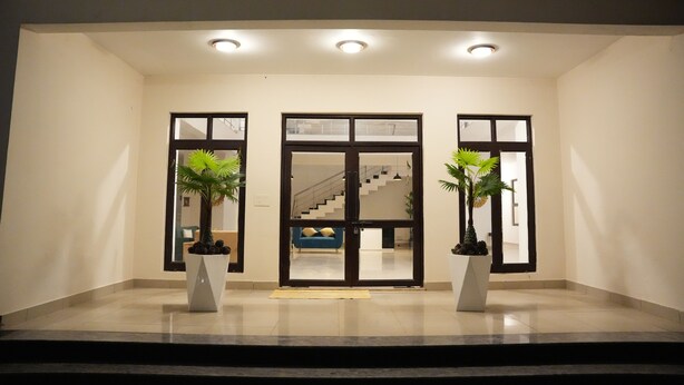 Um hall de hotel moderno, com entrada ampla, escadaria e plantas em vasos.