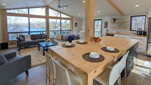 Un vaste espace de vie comprenant une grande table à manger en bois, un canapé et un coin cuisine avec vue sur l’extérieur.