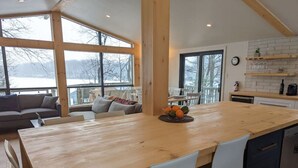 Une cuisine spacieuse avec une grande table en bois, des chaises blanches et une vue sur un paysage enneigé par de grandes fenêtres.
