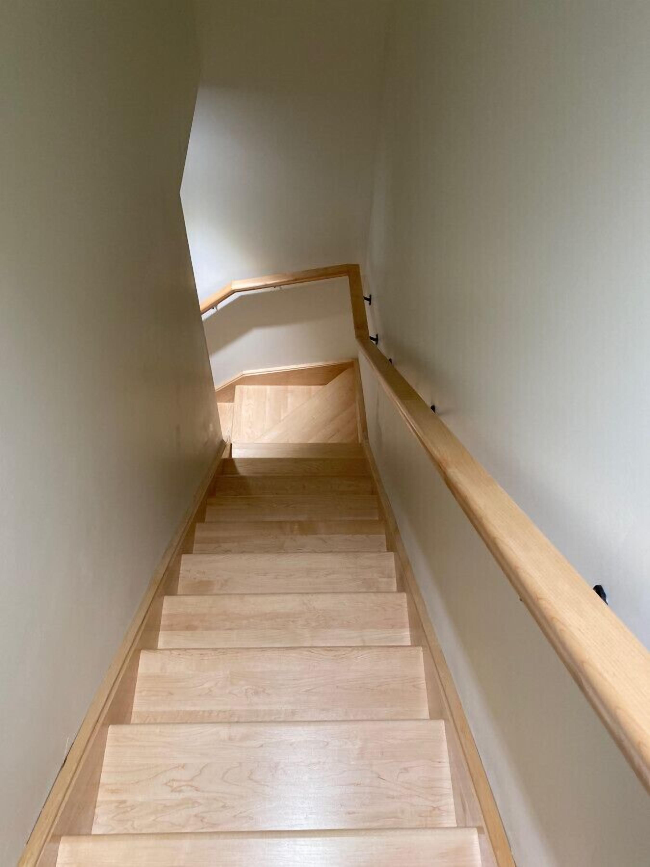 A wooden staircase with a handrail, leading to a landing with a sloped ceiling.
