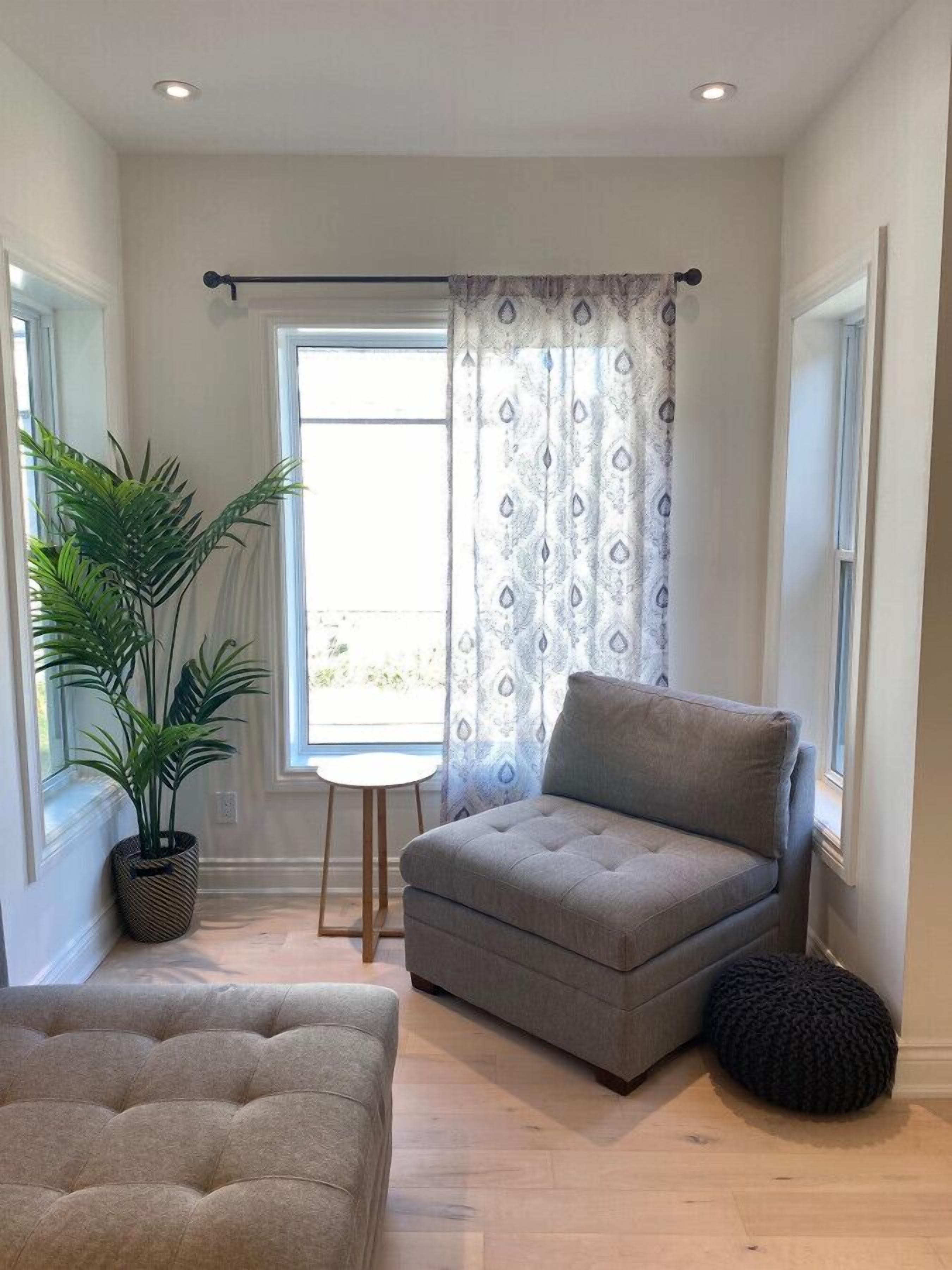 A living room with a grey sofa, a potted plant, and a round ottoman.