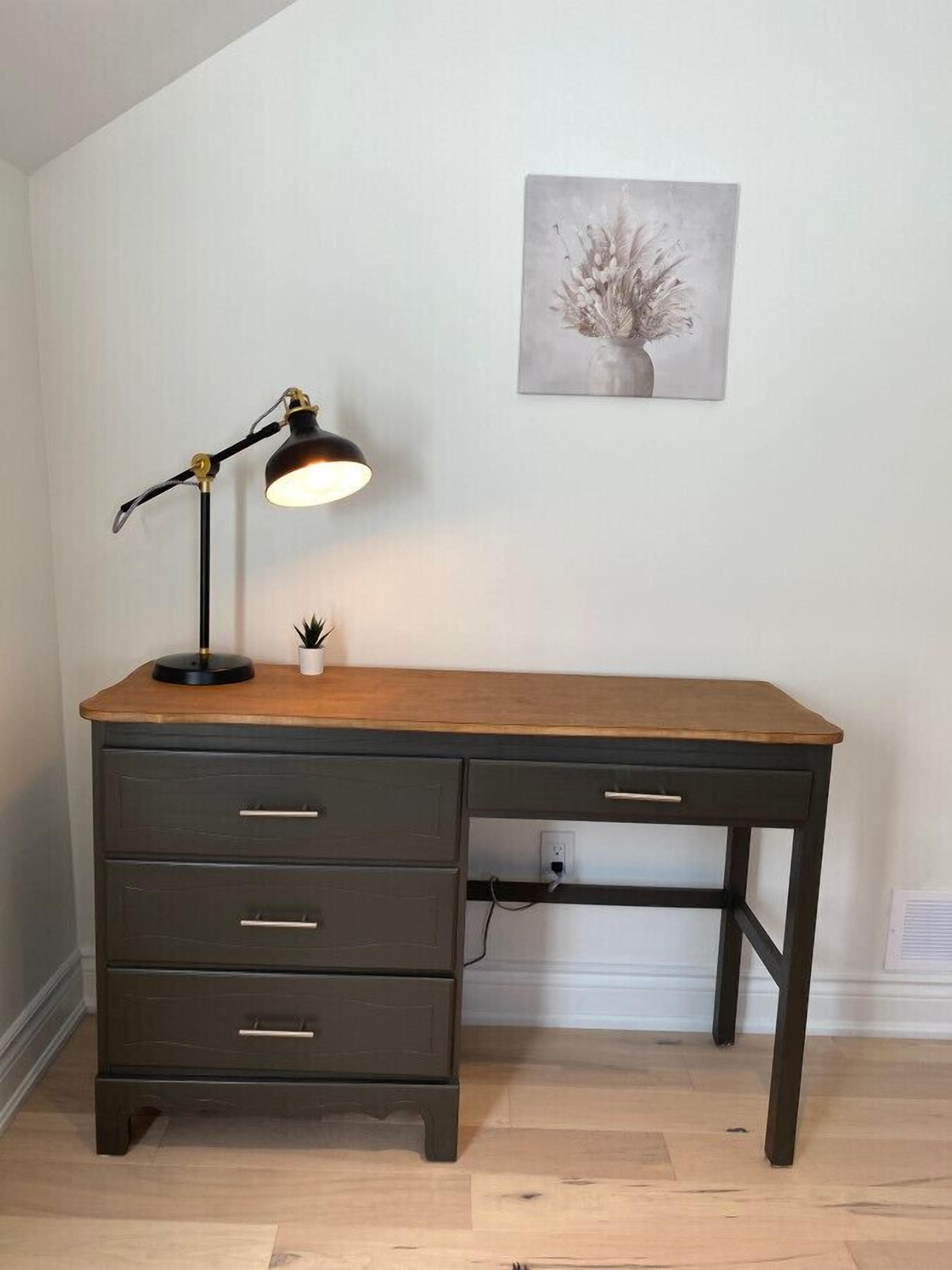 A desk with a lamp, a small plant, and a painting on the wall.