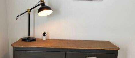 A desk with a lamp, a small plant, and a painting on the wall.