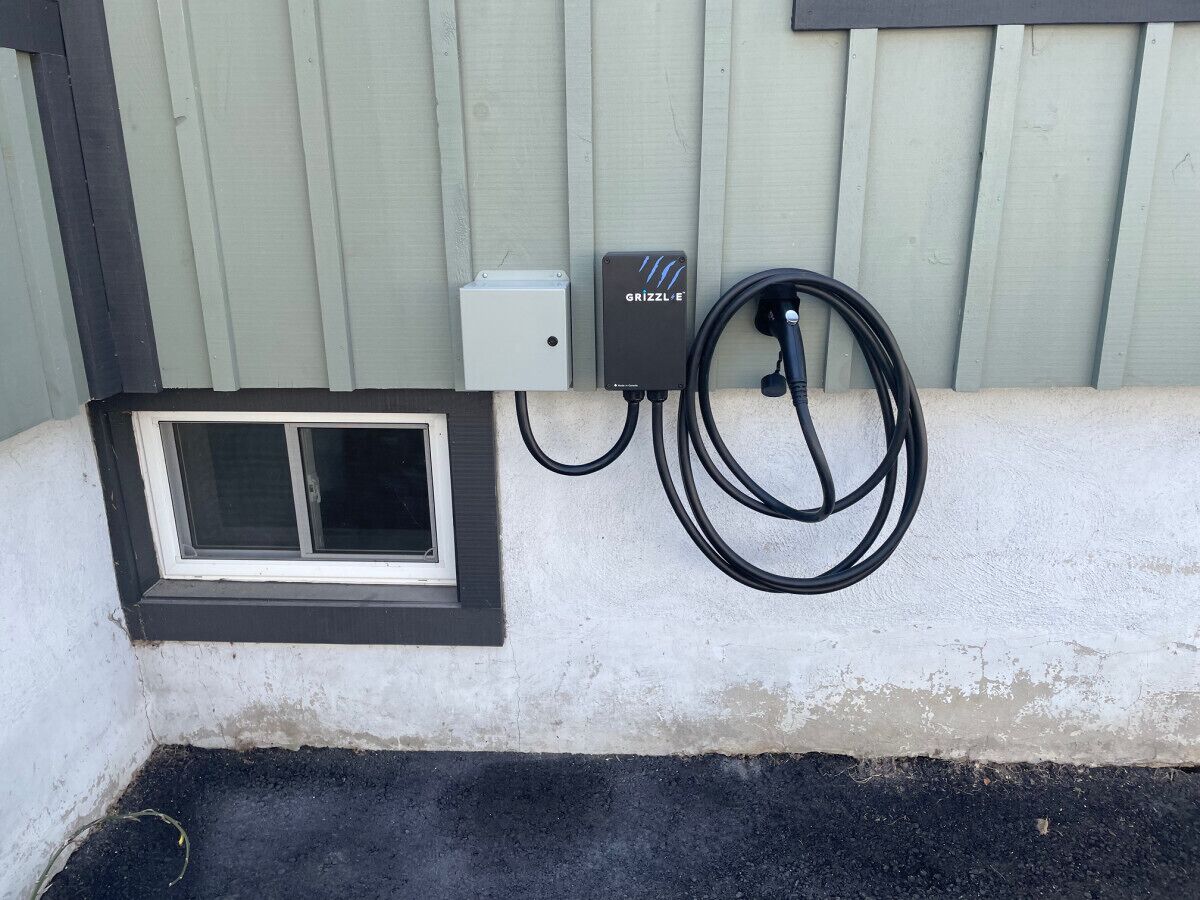 A window with a black frame and a small vent, a power outlet, and a black extension cord on a wall.
