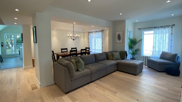 A spacious living room with a large grey sectional sofa, a smaller grey sofa, and a dining area with a table and chairs. - Downtown Picton, 3 bedroom. (Prince Edward)