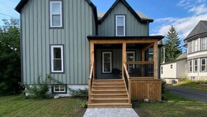 A two-story house with a wooden front porch and a paved walkway leading to the door. - Downtown Picton, 3 bedroom. (Prince Edward)