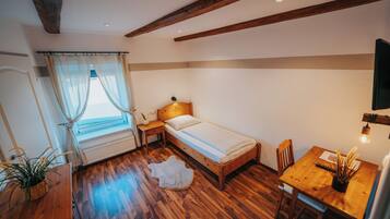 A bedroom with a wooden bed, a small table, a chair, a window with curtains, and a plant.