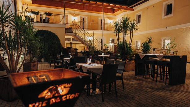 An outdoor dining area with tables and chairs, a fire pit, and potted plants. - Hotel Leo (Steyr)