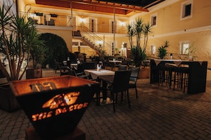 An outdoor dining area with tables and chairs, a fire pit, and potted plants.