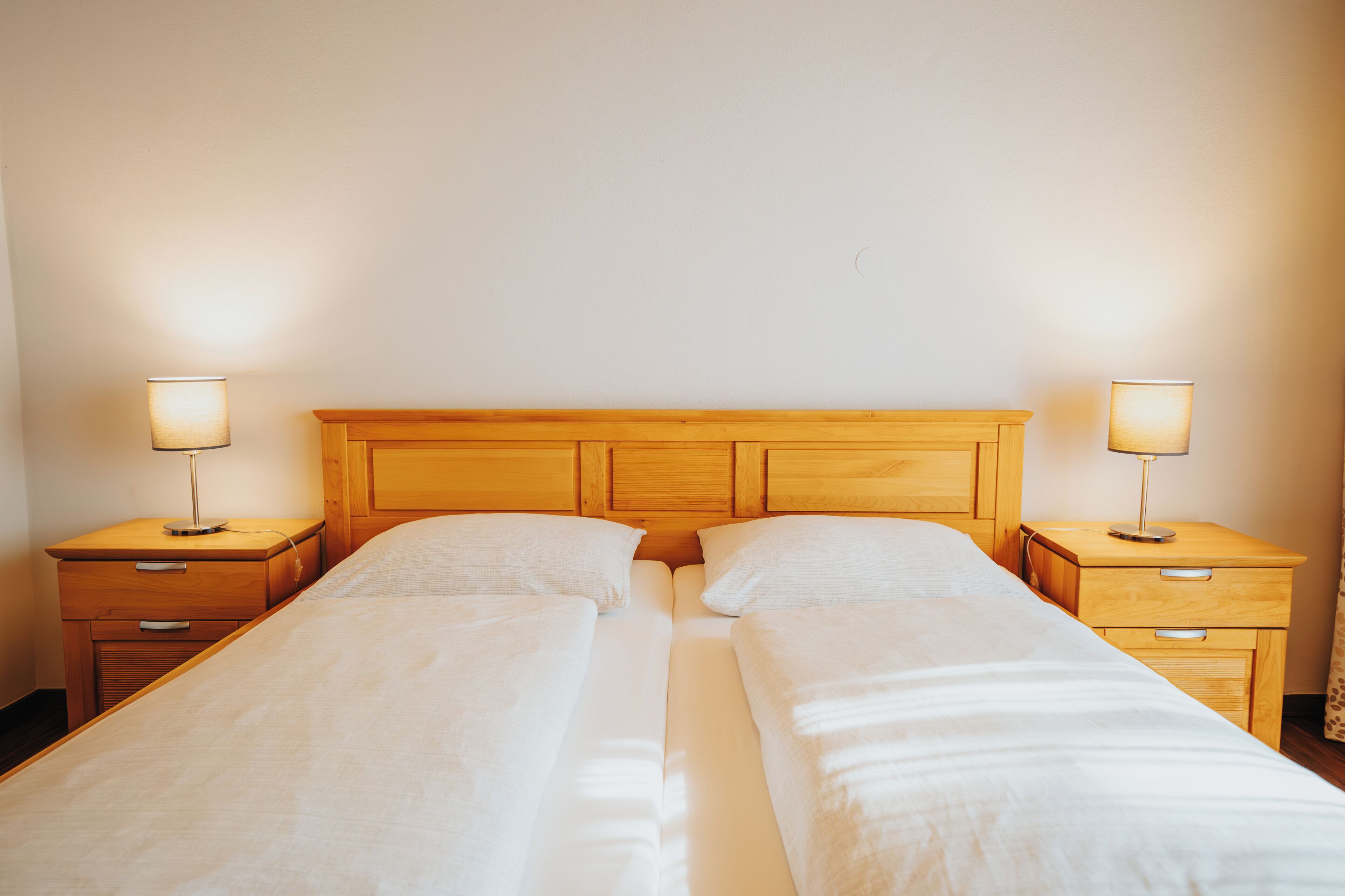Cama doble con cabecera de madera y mesitas de noche a ambos lados.