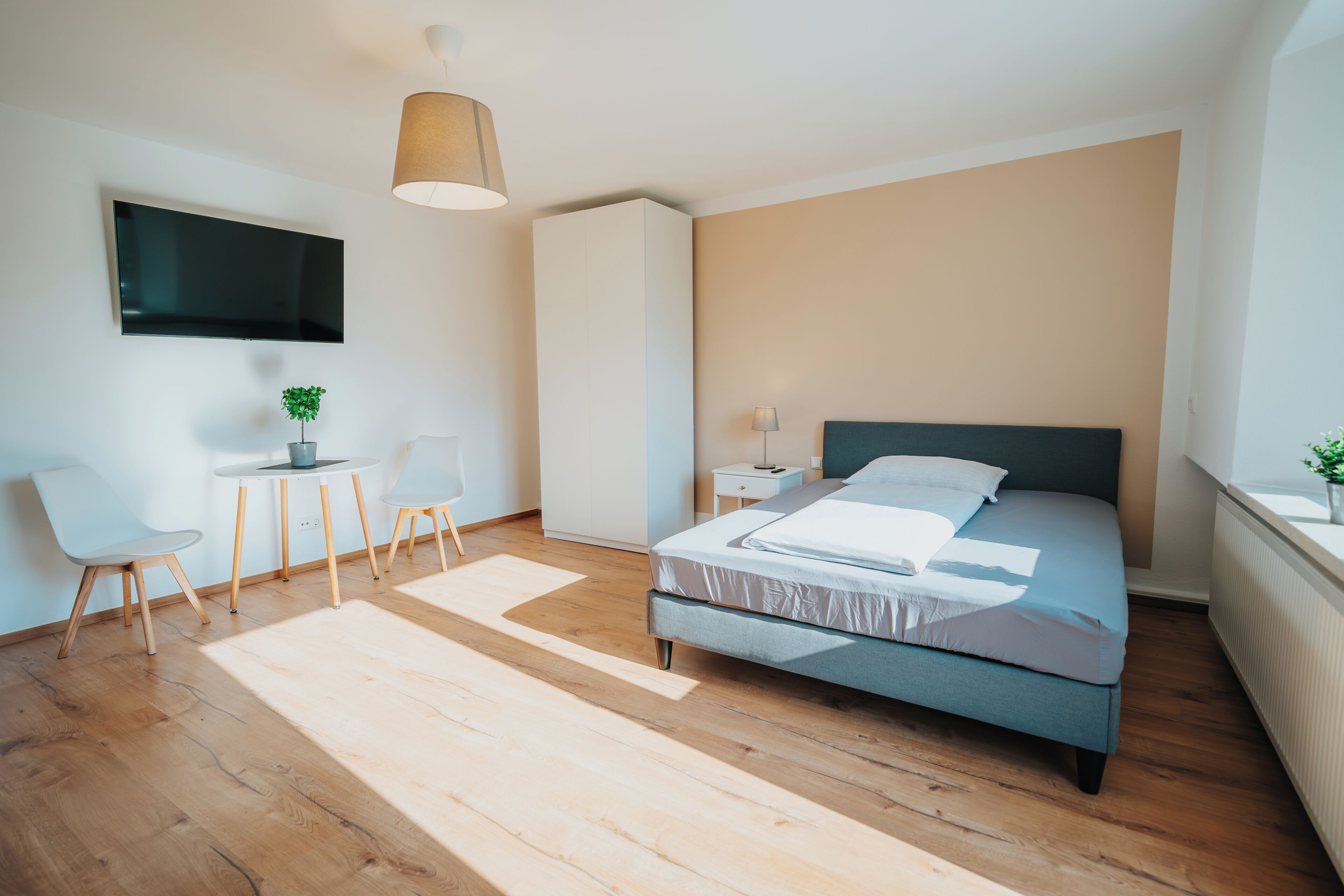 Un dormitorio moderno con cama, escritorio, sillas, televisor y planta.