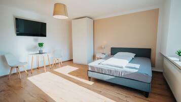 Un dormitorio moderno con cama, escritorio, sillas, televisor y planta.