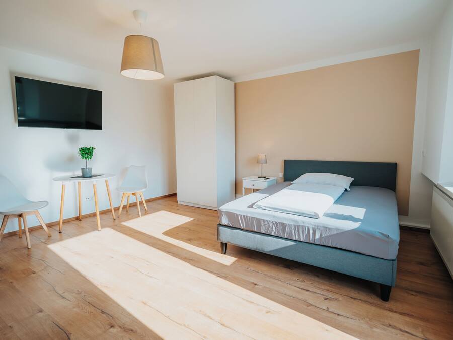 Un dormitorio moderno con cama, escritorio, sillas, televisor y planta.