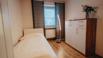 Ett litet sovrum med en säng, ett träskåp och ett element.