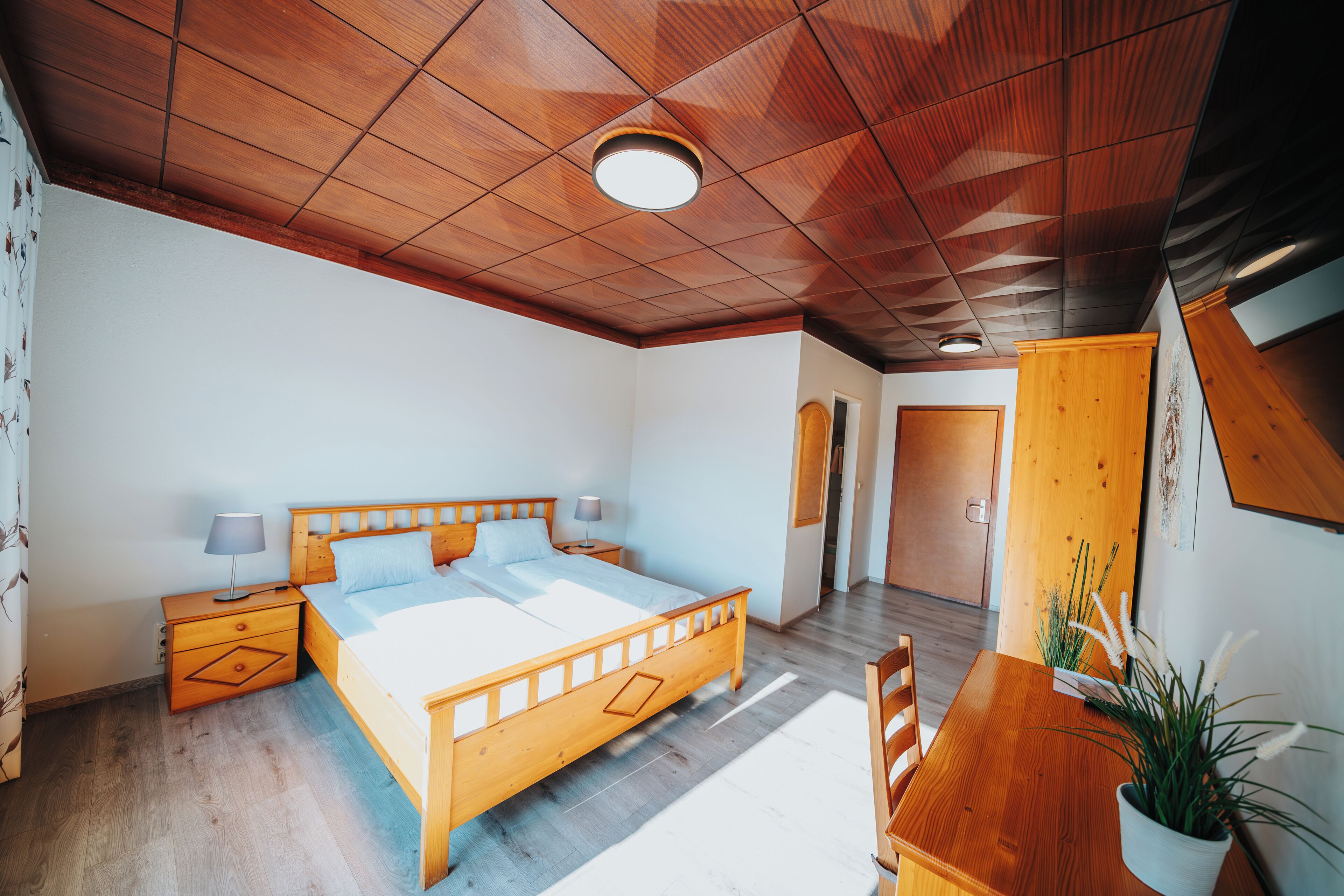 Un dormitorio con cama de madera, mesitas de noche, una mesa de comedor de madera y una planta en maceta.