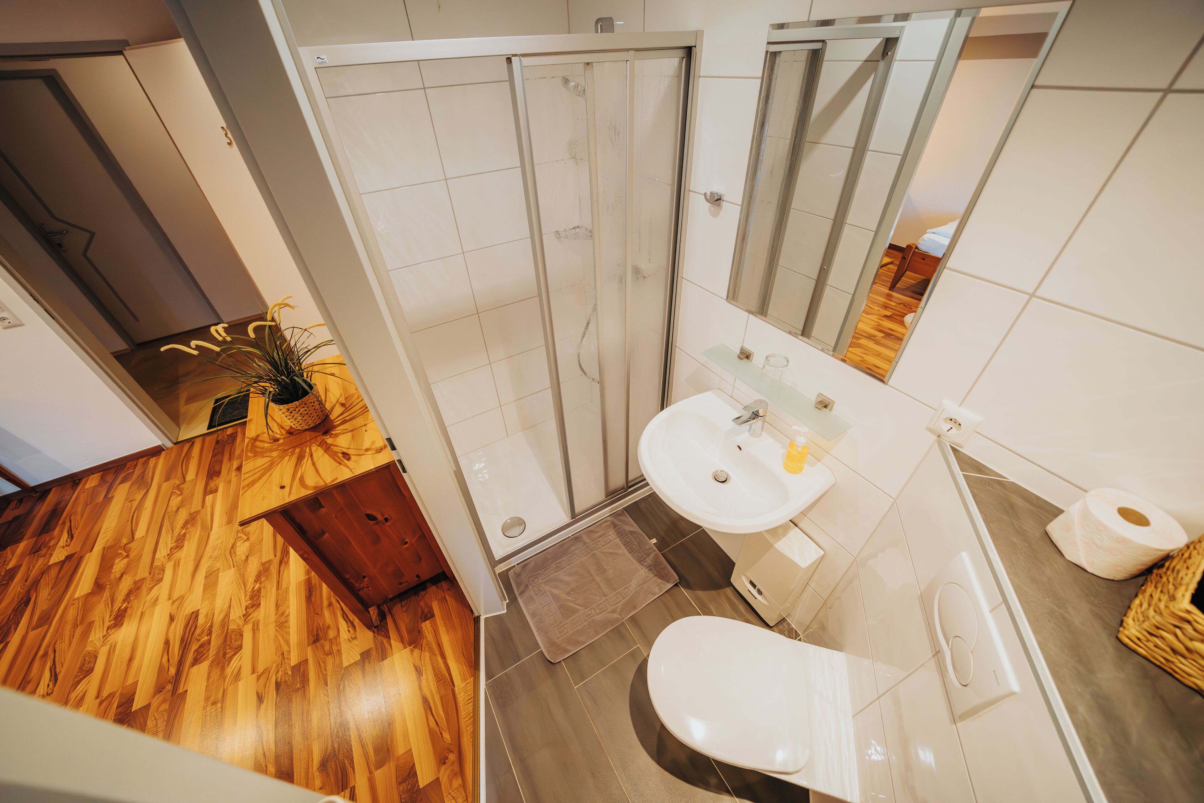 A modern bathroom with a wooden floor, a shower, a sink, and a toilet.