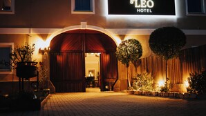 A hotel entrance with a large arched doorway, a signboard above, and potted plants along the pathway. - Hotel Leo (Steyr)