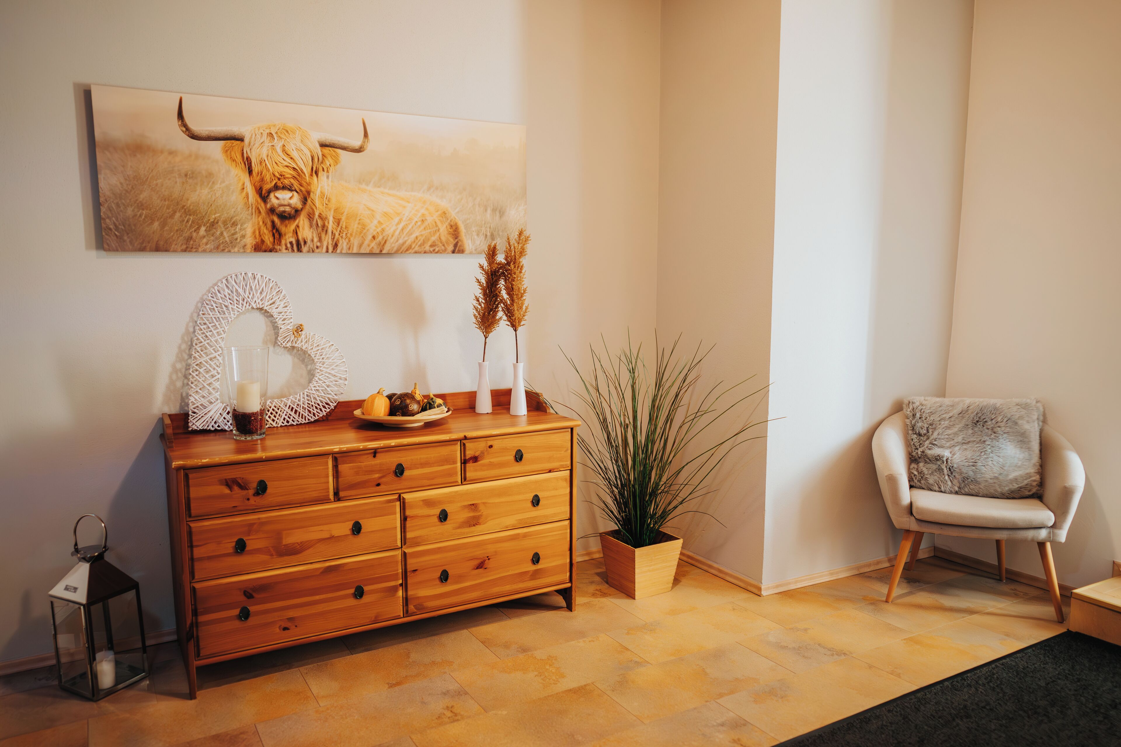 Un aparador de madera con cajones, una planta en maceta, una silla y una obra de arte enmarcada en la pared.