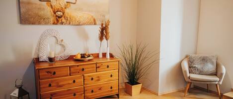 Un aparador de madera con cajones, una planta en maceta, una silla y una obra de arte enmarcada en la pared.