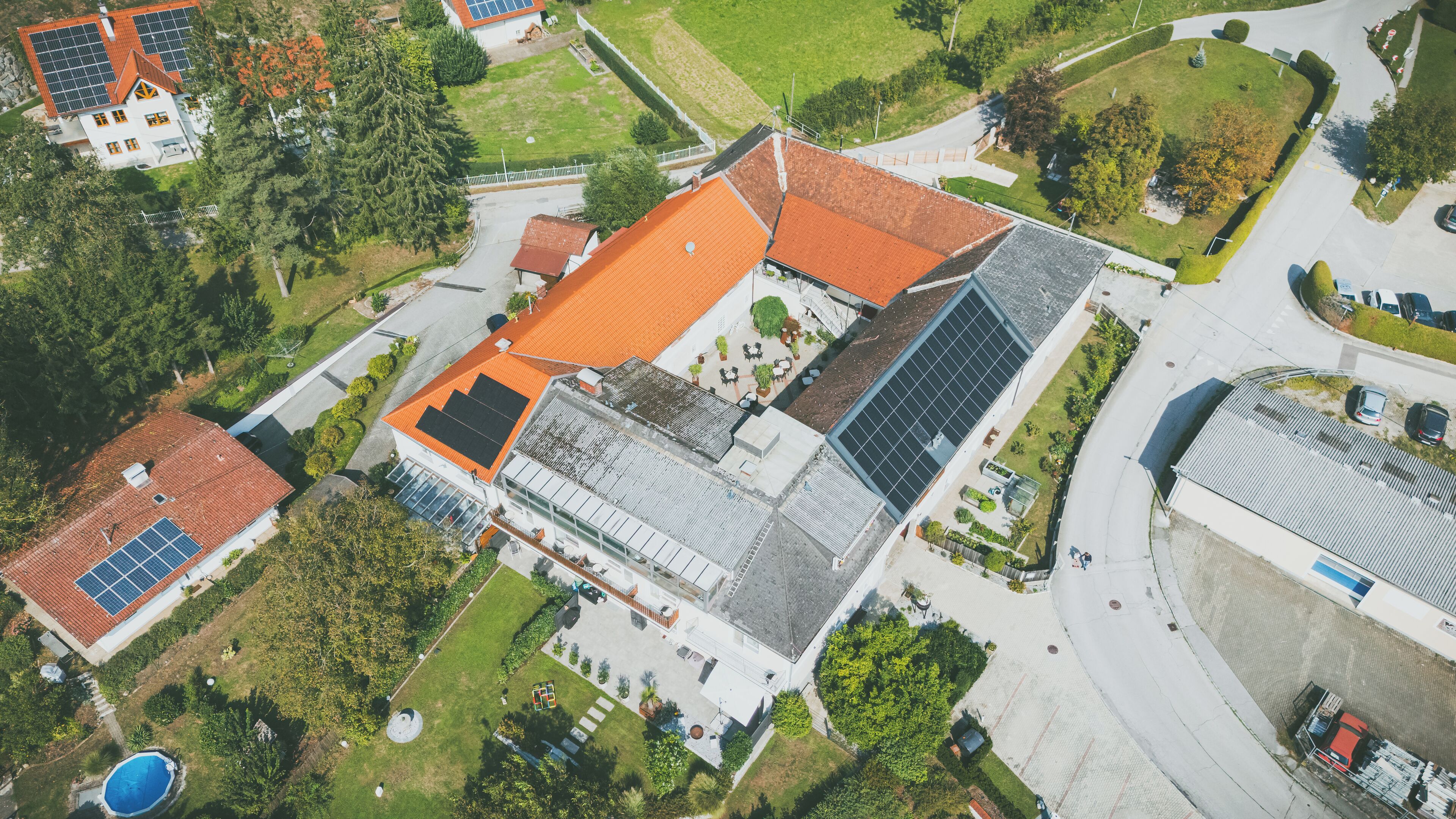 Vista aérea de un barrio residencial con una casa que tiene techo rojo, paneles solares y una piscina.