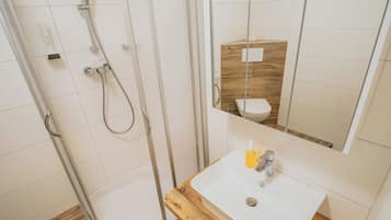 Un baño con ducha envuelta en vidrio, tocador de madera y espejo.