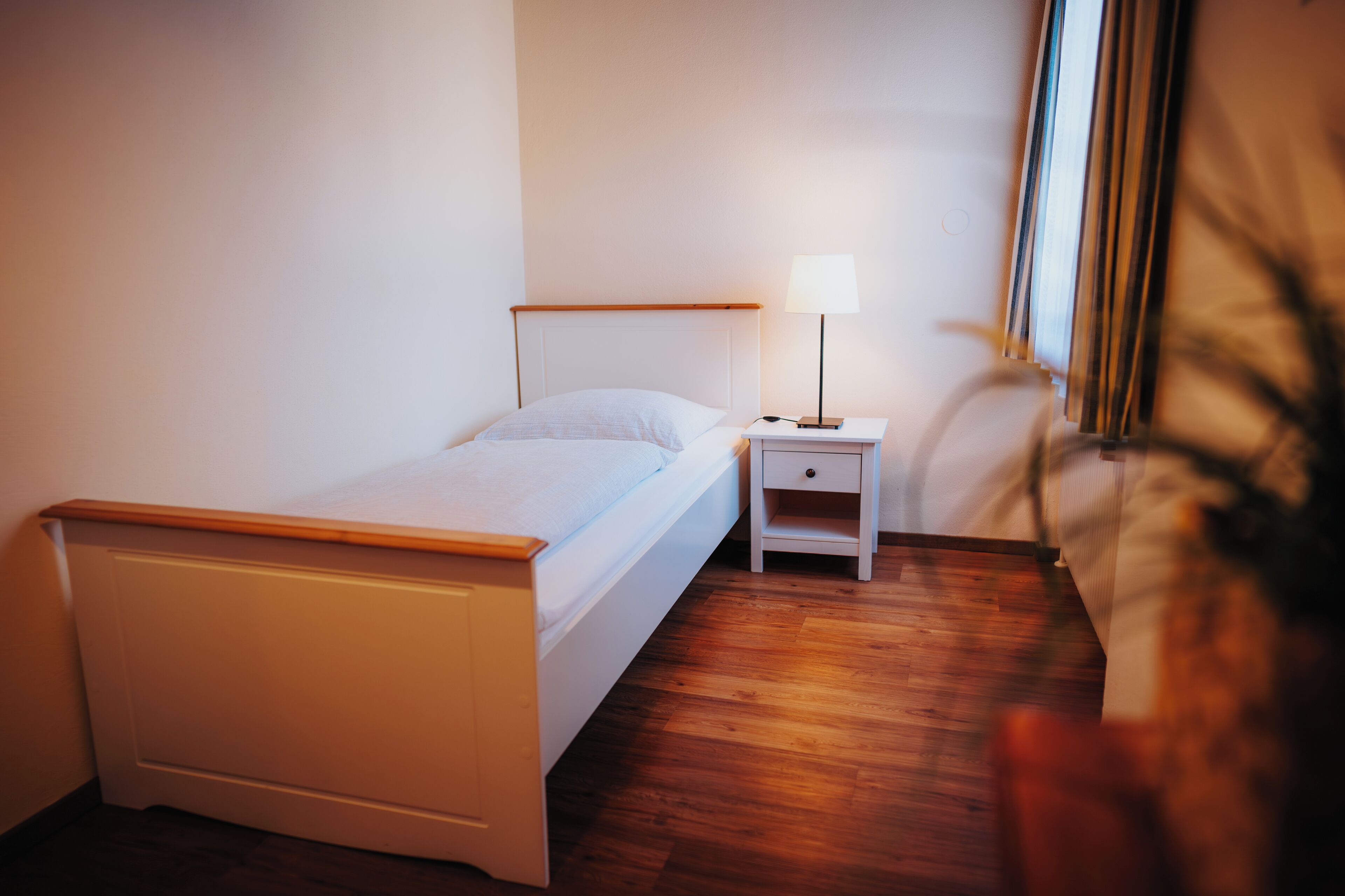 Un dormitorio ordenado con una cama individual, una mesita de noche con lámpara y una pequeña mesa auxiliar.