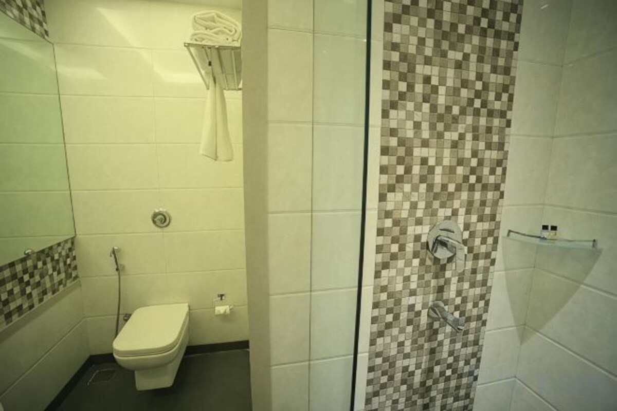 Un baño con inodoro, ducha con pared de cuadros y un perchero.