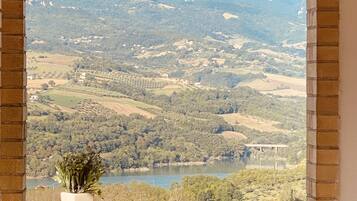 A view from a window overlooking a valley with a lake, distant mountains, and a bridge.
