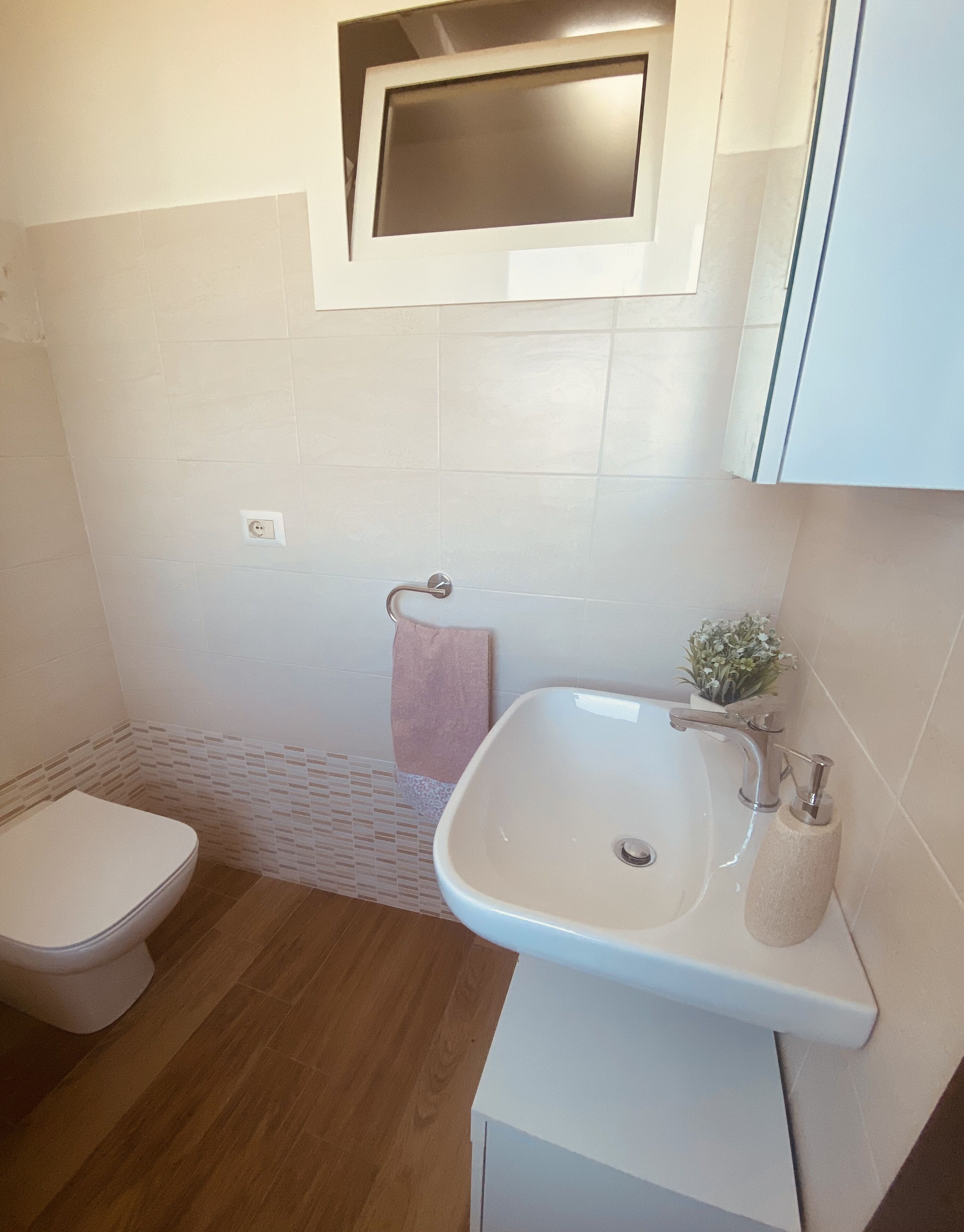 Une salle de bain avec des toilettes, un lavabo et une petite fenêtre située au-dessus du lavabo.