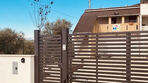 Een omheinde ingang met een metalen poort, een gebouw van baksteen met een bord waarop staat 