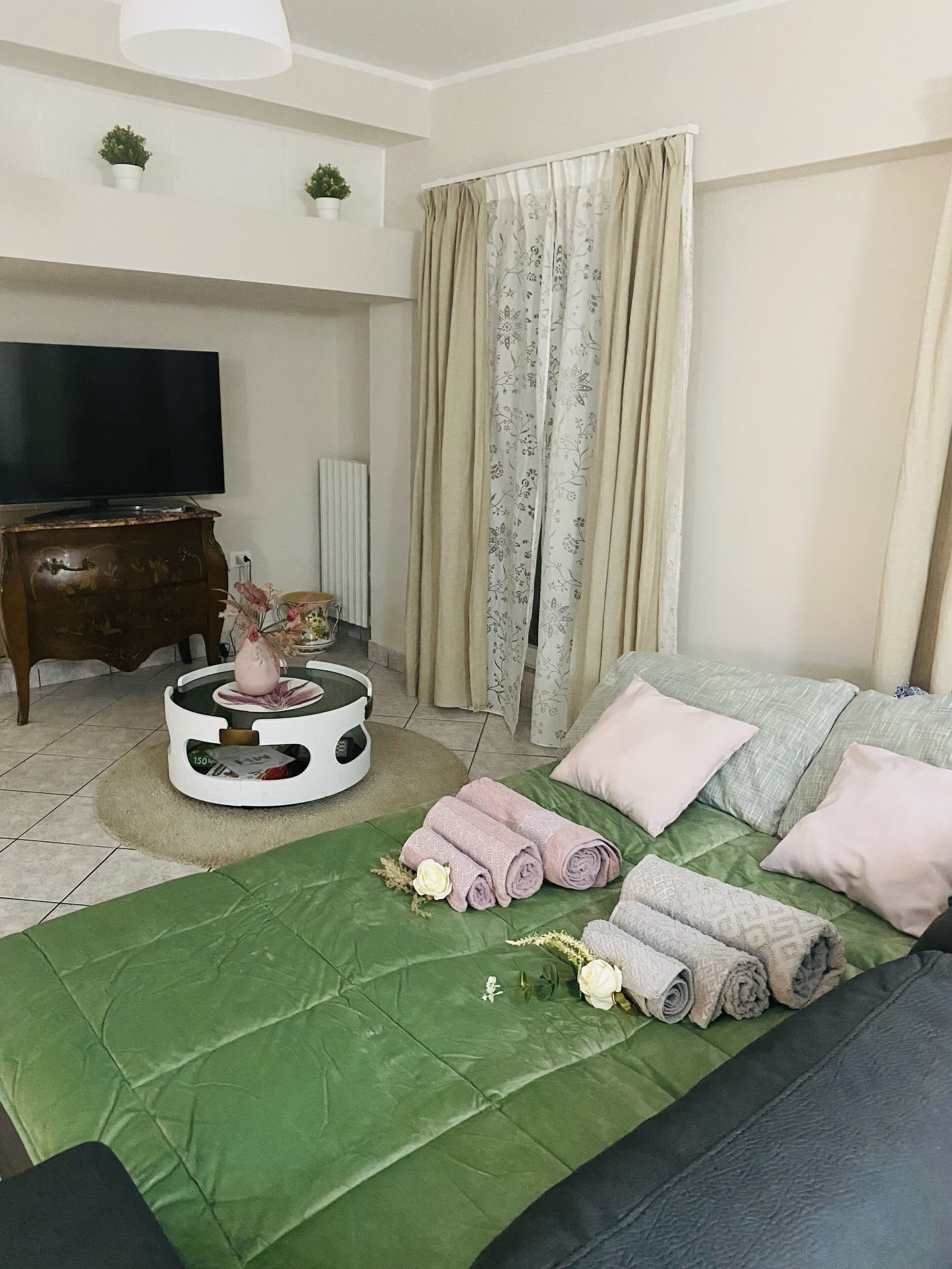 A modern bedroom with a green bed, a television, a white coffee table, and a window with curtains.