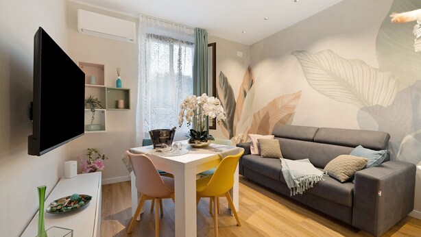 A modern living room with a flat-screen TV, a dining table with chairs, a sofa, and decorative plants. - Apartment 'Soleluna' with Wi-Fi and Air Conditioning (Vado Ligure)