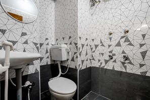 Une salle de bain comprenant des toilettes, un lavabo et un miroir. Les murs sont recouverts de carreaux disposés selon un motif géométrique.