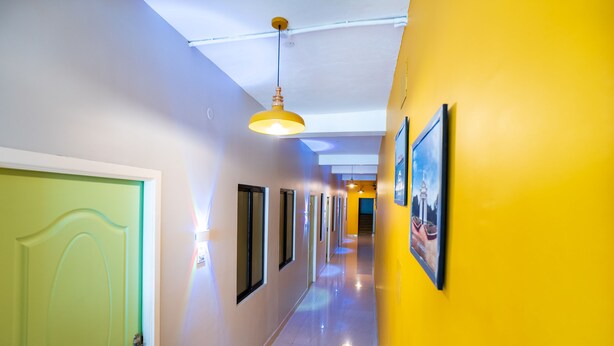 A hallway with a green door, yellow walls, and framed pictures on the right. - Hotel Les Hues (Puducherry)