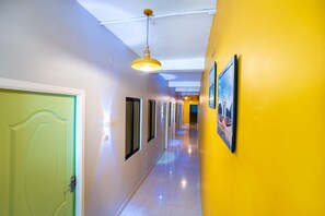 A hallway with a green door, yellow walls, and framed pictures on the right. - Hotel Les Hues (Puducherry)