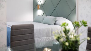 Quarto moderno com uma cama, mesa de cabeceira, vaso com flores e luminária na parede.