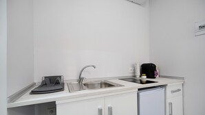 Uma cozinha compacta equipada com pia, pequena geladeira e bancada com chaleira e cafeteira.