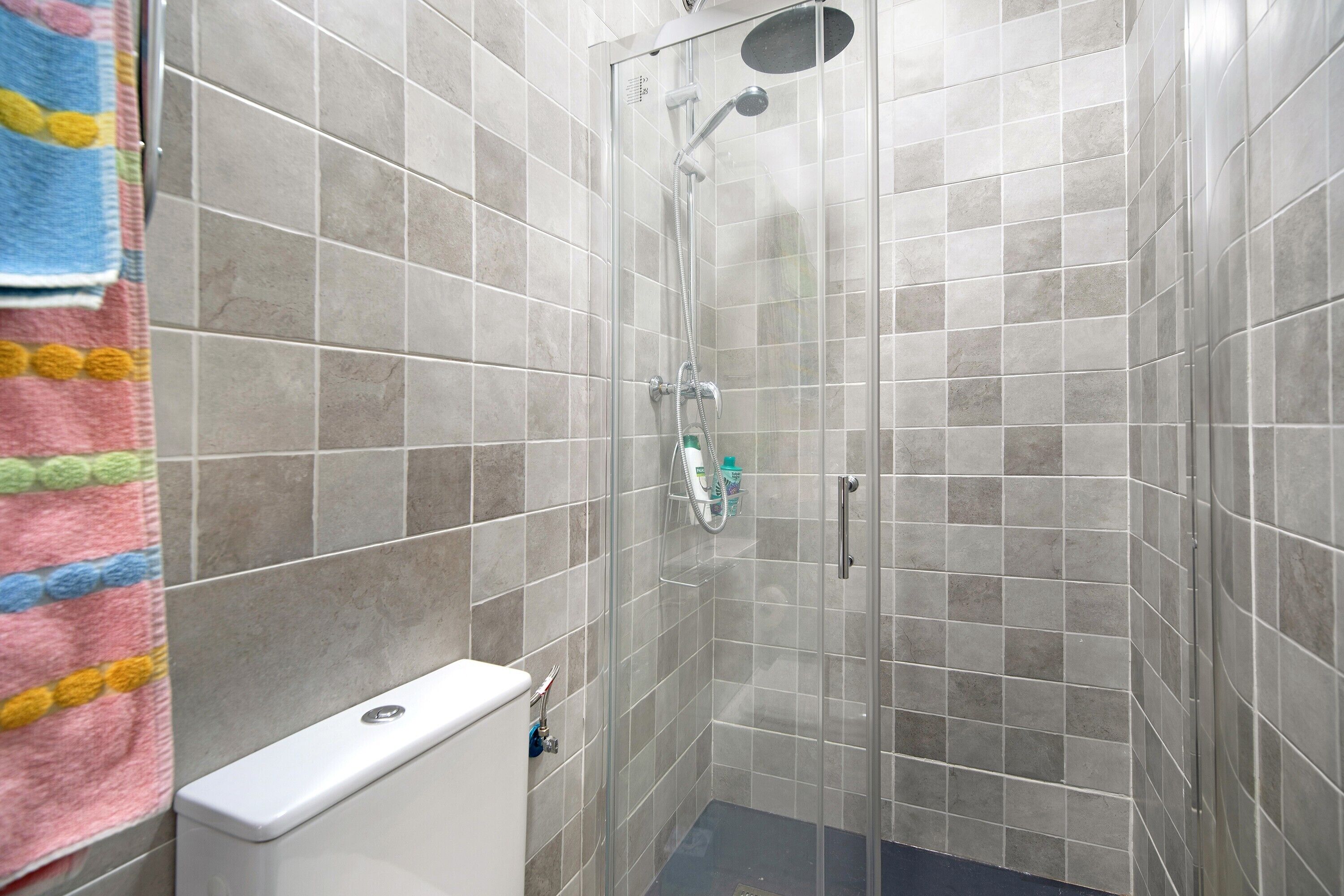 Eine Dusche mit Glastür, eine Toilette und ein Handtuchhalter mit bunten Handtüchern.