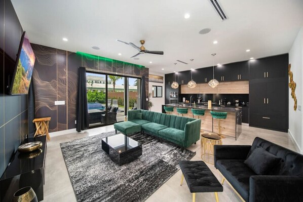 A modern living room with a green sofa, black armchair, and a coffee table. - Elements Luxury Home with Pool and Hot Tub Near the Beach (Fort Lauderdale)