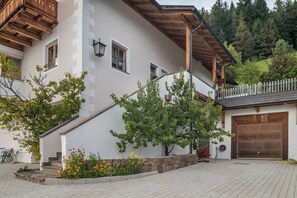 Un bĂątiment blanc avec un escalier en bois, un garage et un mur en pierre.
