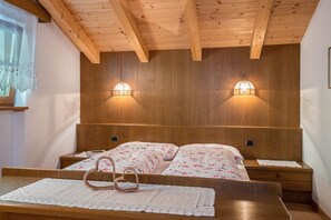 A wooden-paneled bedroom with two bedside tables, a bed with floral bedding, and two wall-mounted lamps.