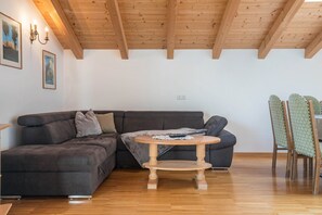 A room with a wooden ceiling, a dark brown sectional sofa, a round wooden table, and a chair with a patterned cushion. - Apartment 'Funtnatsch Schlern' with Mountain View, Shared Terrace and Wi-Fi (Laion)
