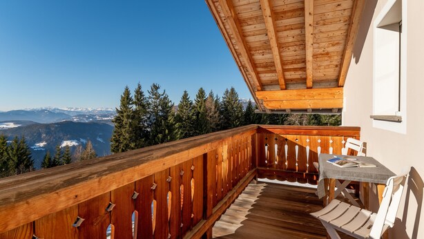 Un balcón de madera con una mesa y sillas, con vistas a un paisaje montañoso.