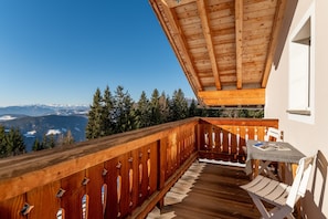 Ein Holzbalkon mit Tisch und Stühlen, mit Blick auf eine gebirgige Landschaft.