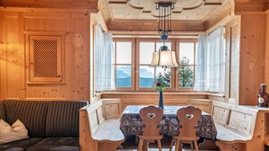 A wooden cabin interior with a sofa, bench seating, a table, and a view of mountains through large windows.