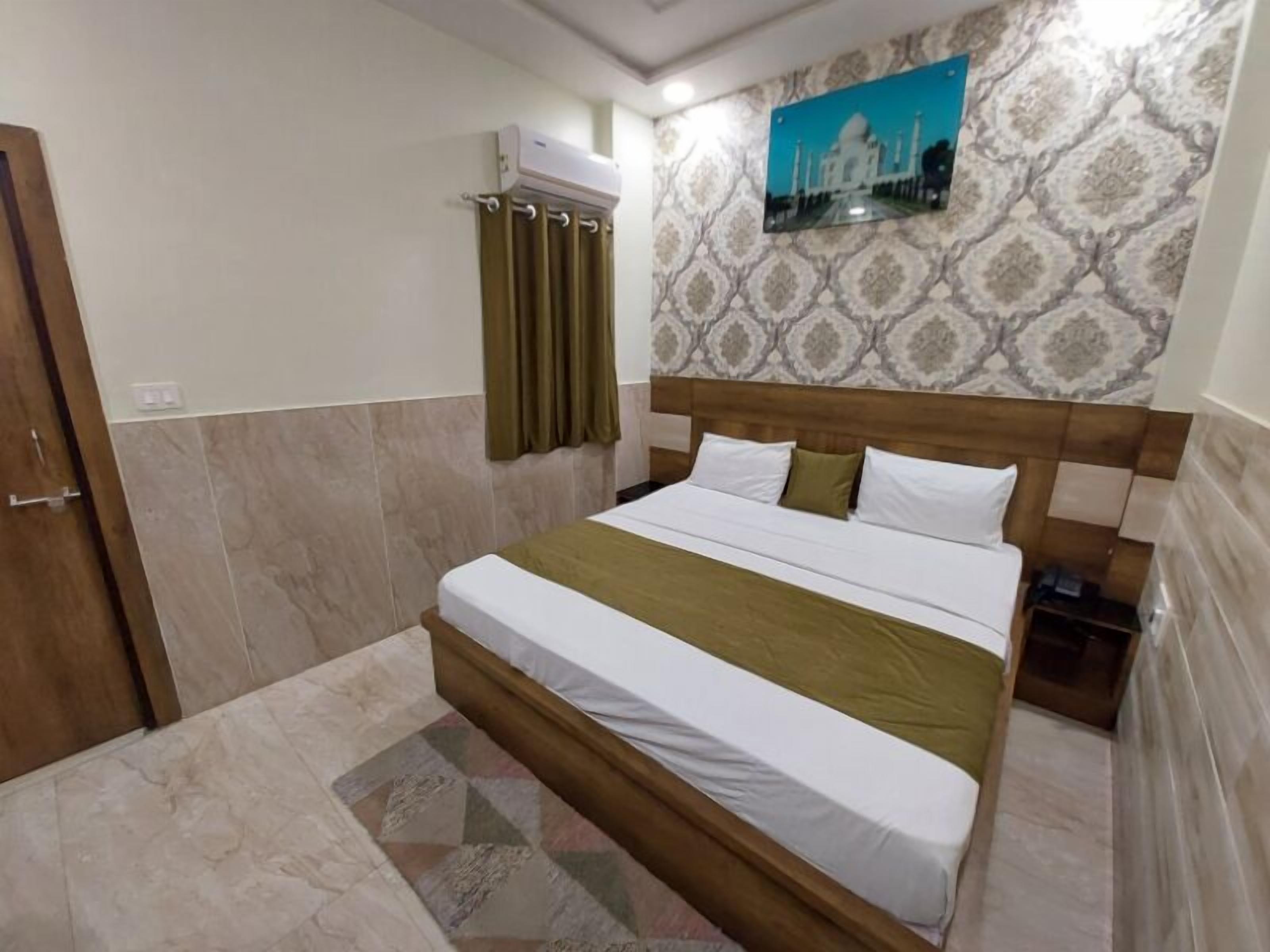 Hotelkamer met een groot bed, een wandairconditioner, behang met een patroon en een ingelijst beeld van de Taj Mahal.